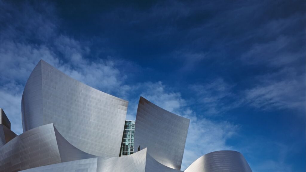 Curved metallic panels of a modern building, set against a vivid blue sky with wispy clouds.