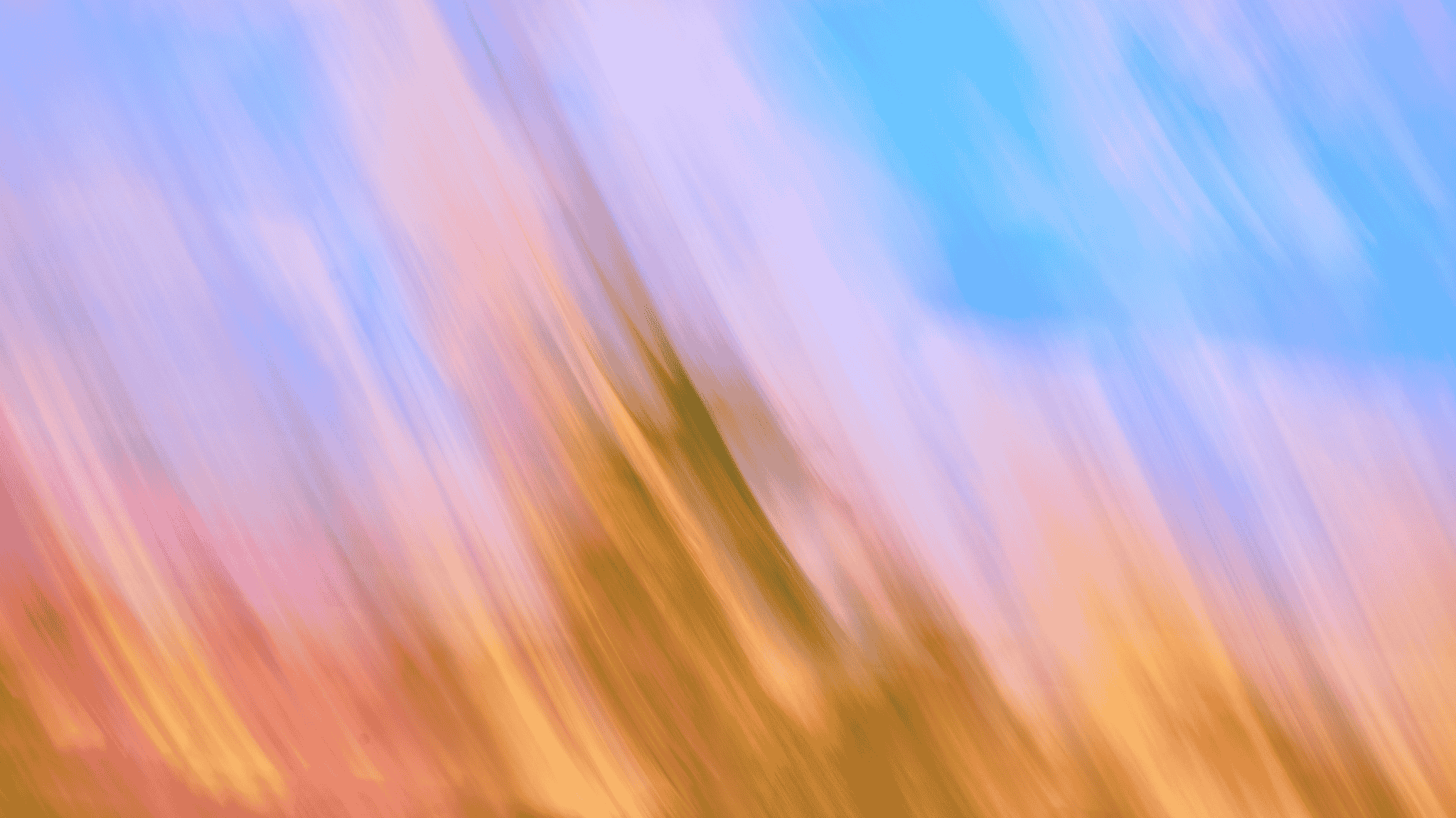 Abstract image featuring diagonal streaks of orange, pink, and yellow blending into a background of blue and light purple, creating a dynamic, colorful pattern.