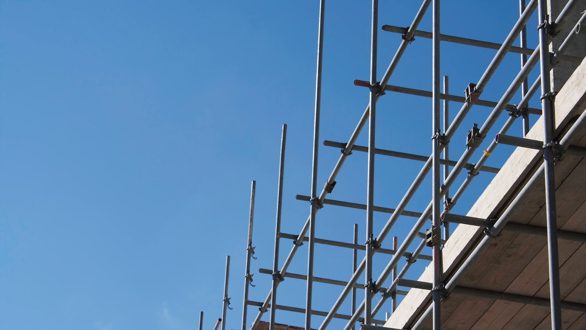 Metal scaffolding against a clear blue sky, with several horizontal and vertical poles supporting a structure—like guardian agents steadfastly safeguarding a building under construction.