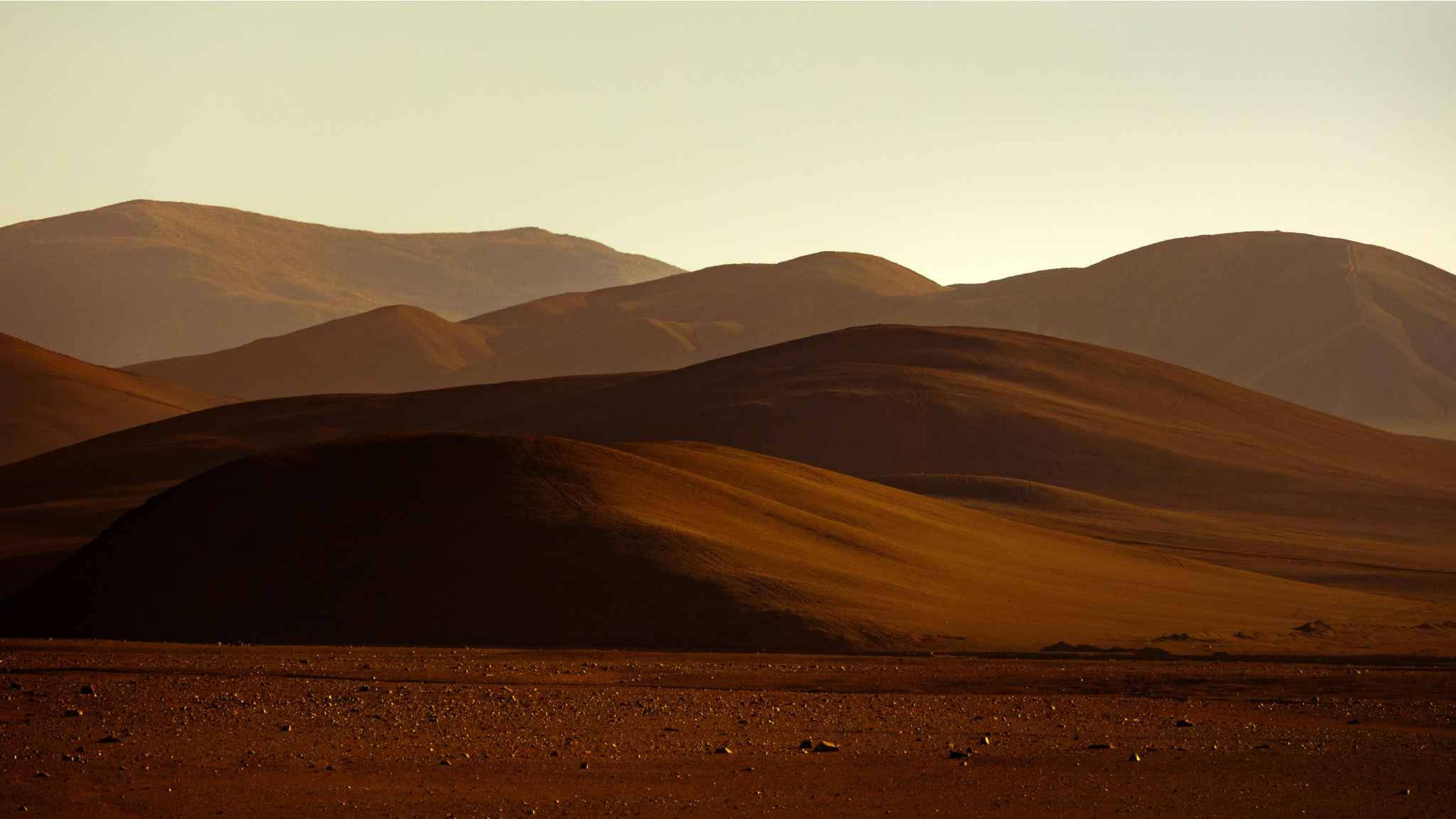 Rolling brown hills under a hazy sky, with soft sunlight highlighting the curves of the landscape and distant mountain ridges in the background.