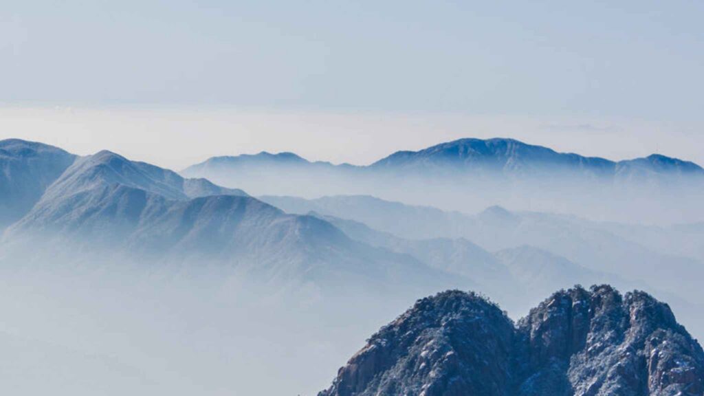 Blue-gray mountain ranges fade into the misty distance under a pale sky, creating a sense of depth and tranquility.