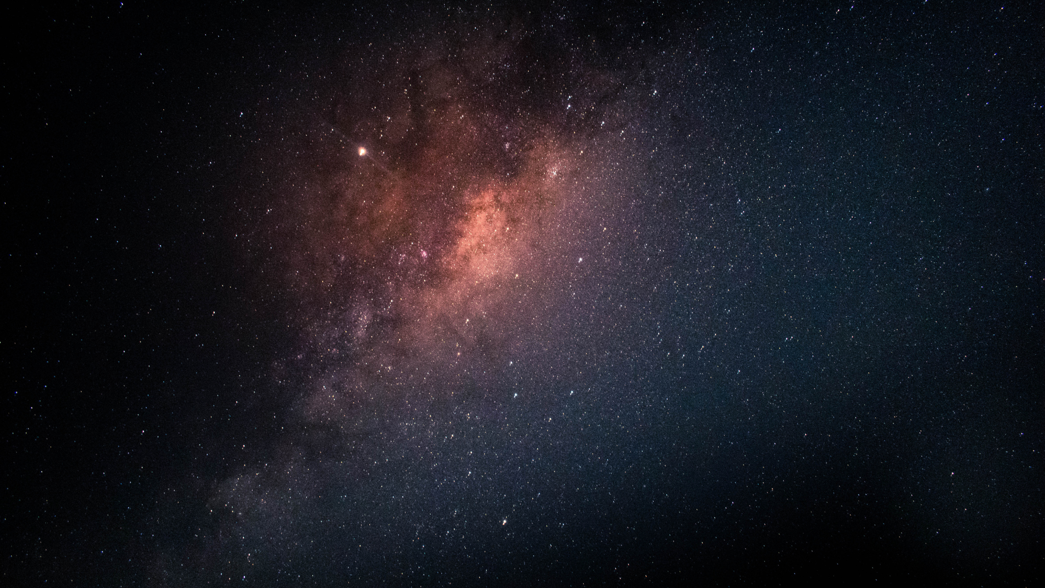A breathtaking view of the Milky Way galaxy set against a deep black night sky, showcasing a dense, glowing band of stars, colorful interstellar dust clouds, and countless sparkling stars extending into the vast darkness of space.