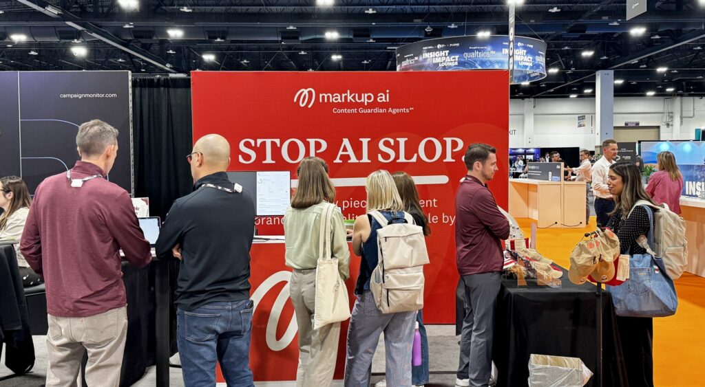 People stand at a red trade show booth branded markup ai with the text STOP AI SLOP displayed in large white letters.
