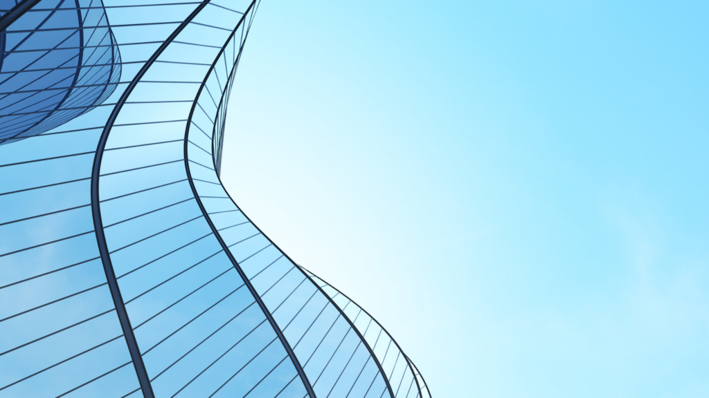 A low-angle view of a modern building with a curved glass facade against a clear blue sky.