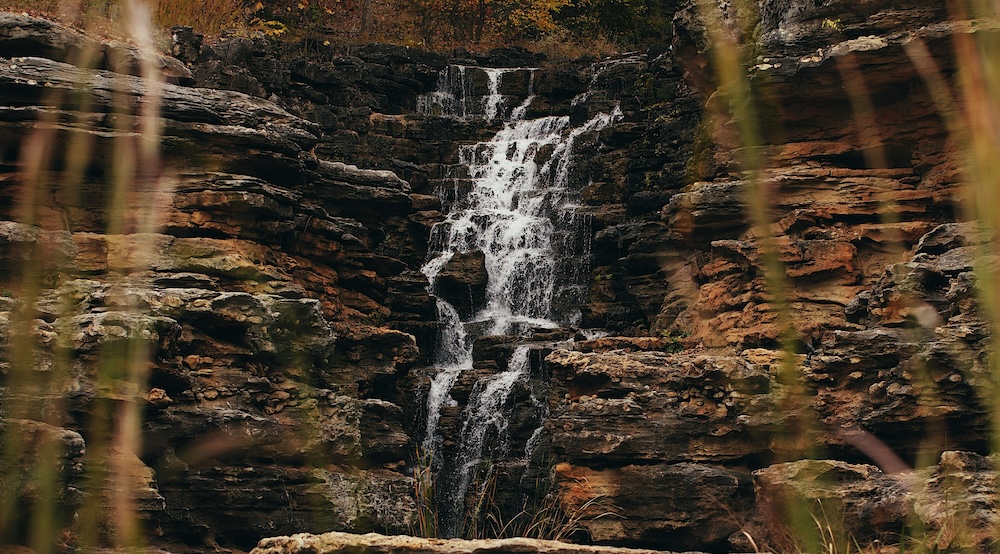 A waterfall flows down a tiered, rocky cliff face captured within a new markup ai editor. connor-wilkins-__m1fle9P_E-unsplash