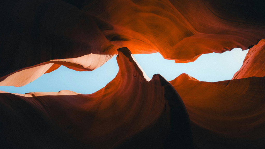 Looking up at the sky through the smooth, orange, wave-like walls of a slot canyon.