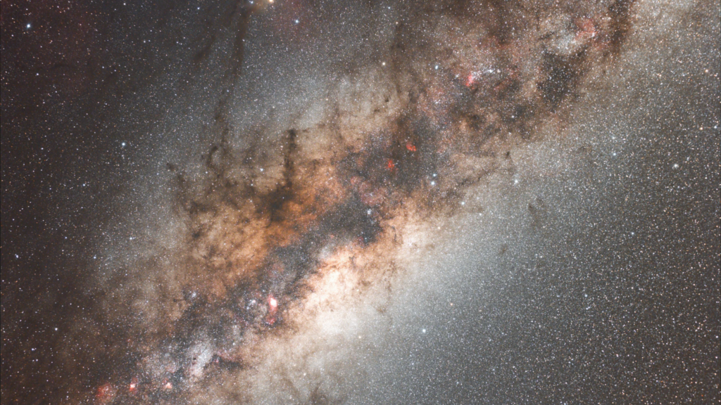 A dense band of the Milky Way galaxy featuring bright star clusters and dark dust lanes stretching across a starry field.